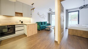 Een moderne keuken met een inbouwoven, houten kasten en een groene bank in de woonkamer.