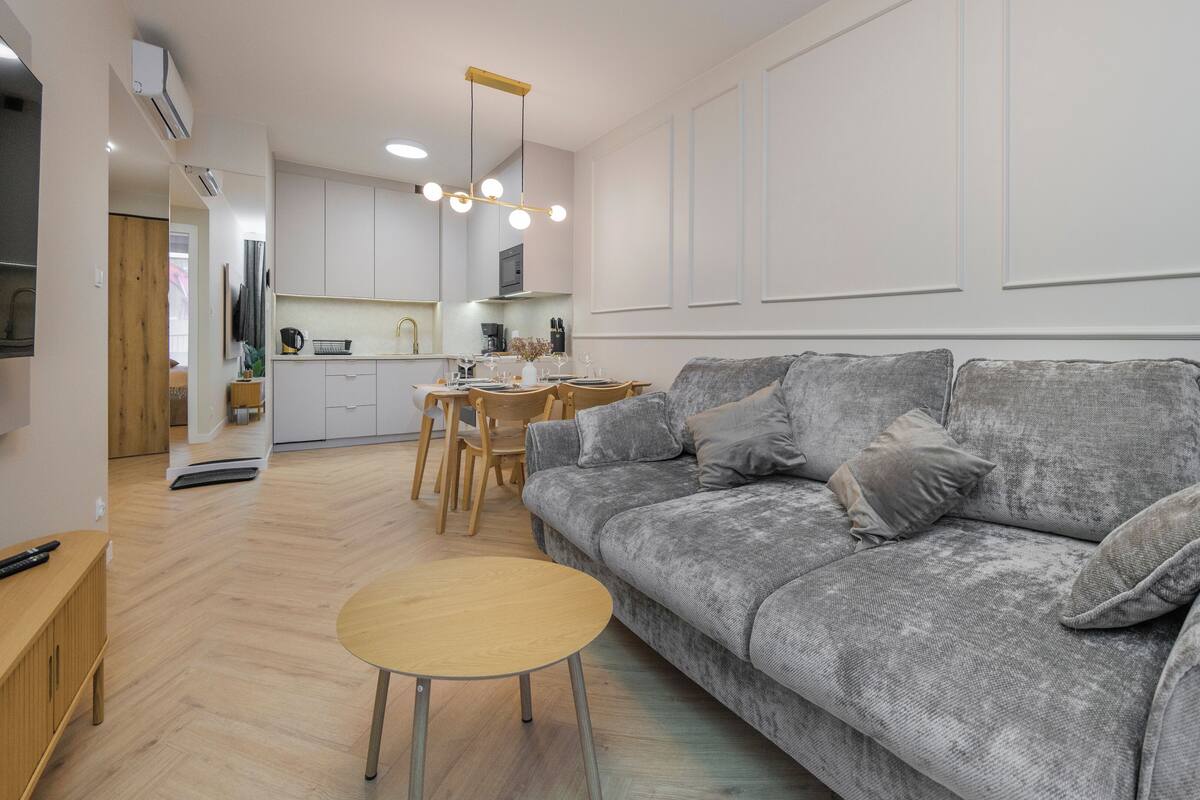 A modern living room with a grey sofa, wooden coffee table, and a dining area with a kitchen in the background.