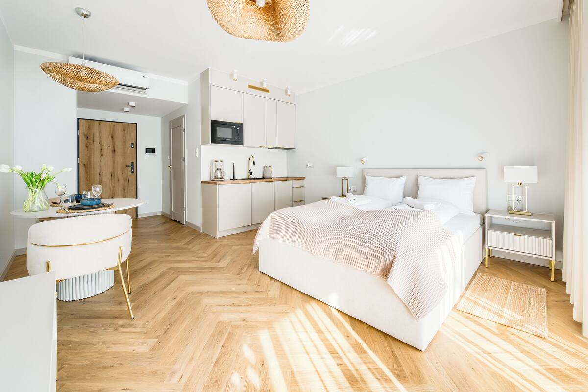 A modern hotel room with a large bed, a kitchenette, a dining area, and a bathroom.
