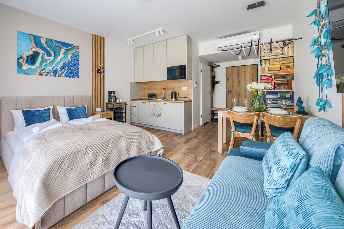 A modern hotel room with a bed, a sitting area, a kitchenette, and a dining area.