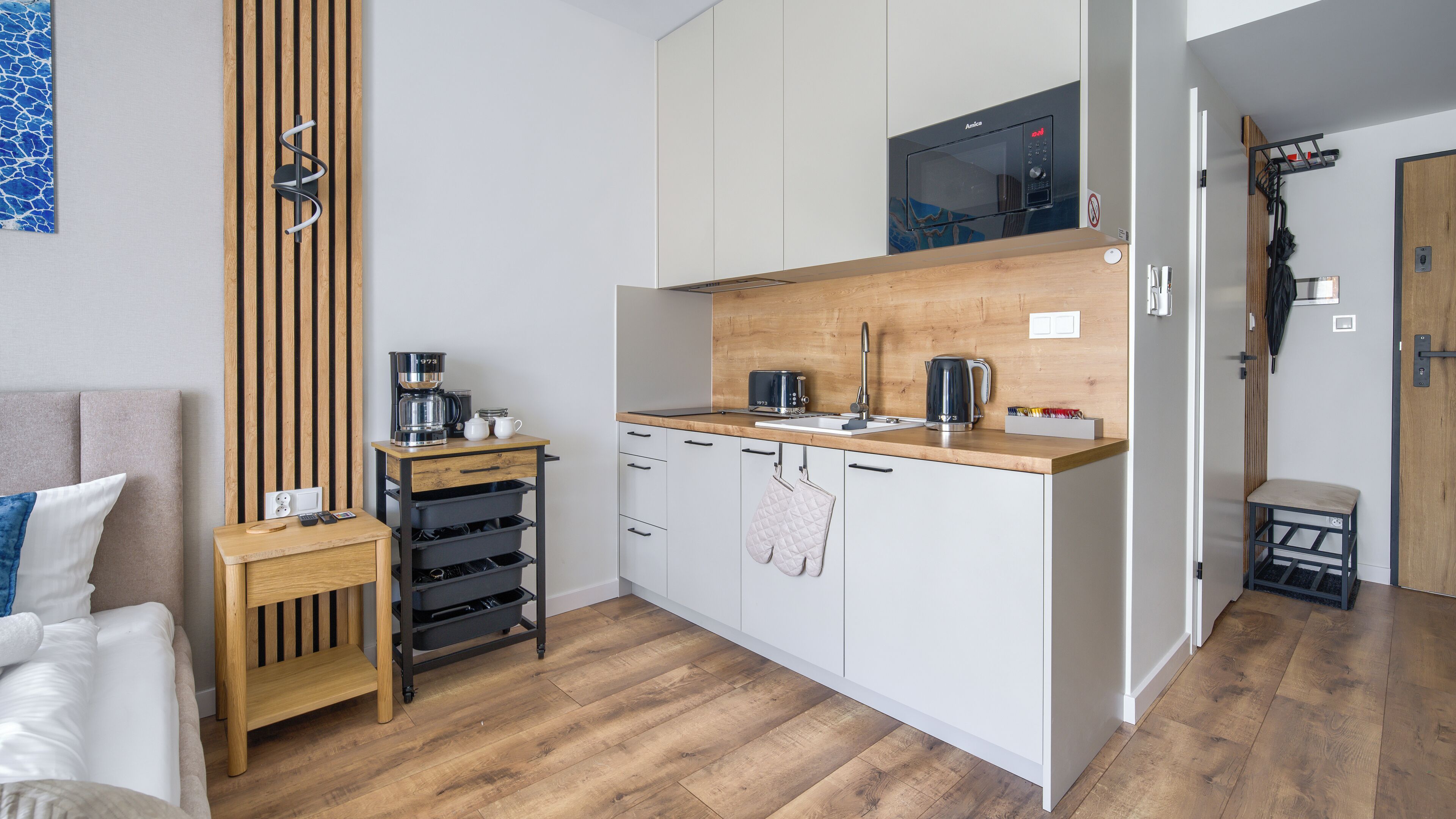 A compact kitchen with a microwave, coffee maker, and toaster. There is a wooden cabinet with a hanging oven mitt.