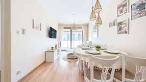 Een eetruimte met een ronde tafel voor zes personen, witte stoelen en uitzicht naar buiten.