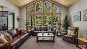 A spacious living room with a large window, a leather sofa, a coffee table, and a leather armchair.
