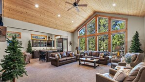 A spacious living area with a high ceiling, large windows, and a cozy fireplace.