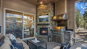 An outdoor patio with a stone fireplace, a TV mounted on the wall, and a grill.