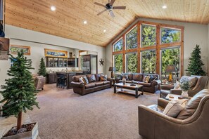 Relax in this inviting living area with a high ceiling, leather sofa, and armchair, offering a view of the surrounding forest.