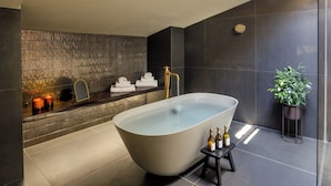 A modern bathroom with a freestanding bathtub, a towel rack with towels, a potted plant, and candles on a shelf. - Palazzo Serpe Suites near Colosseum (Rome)