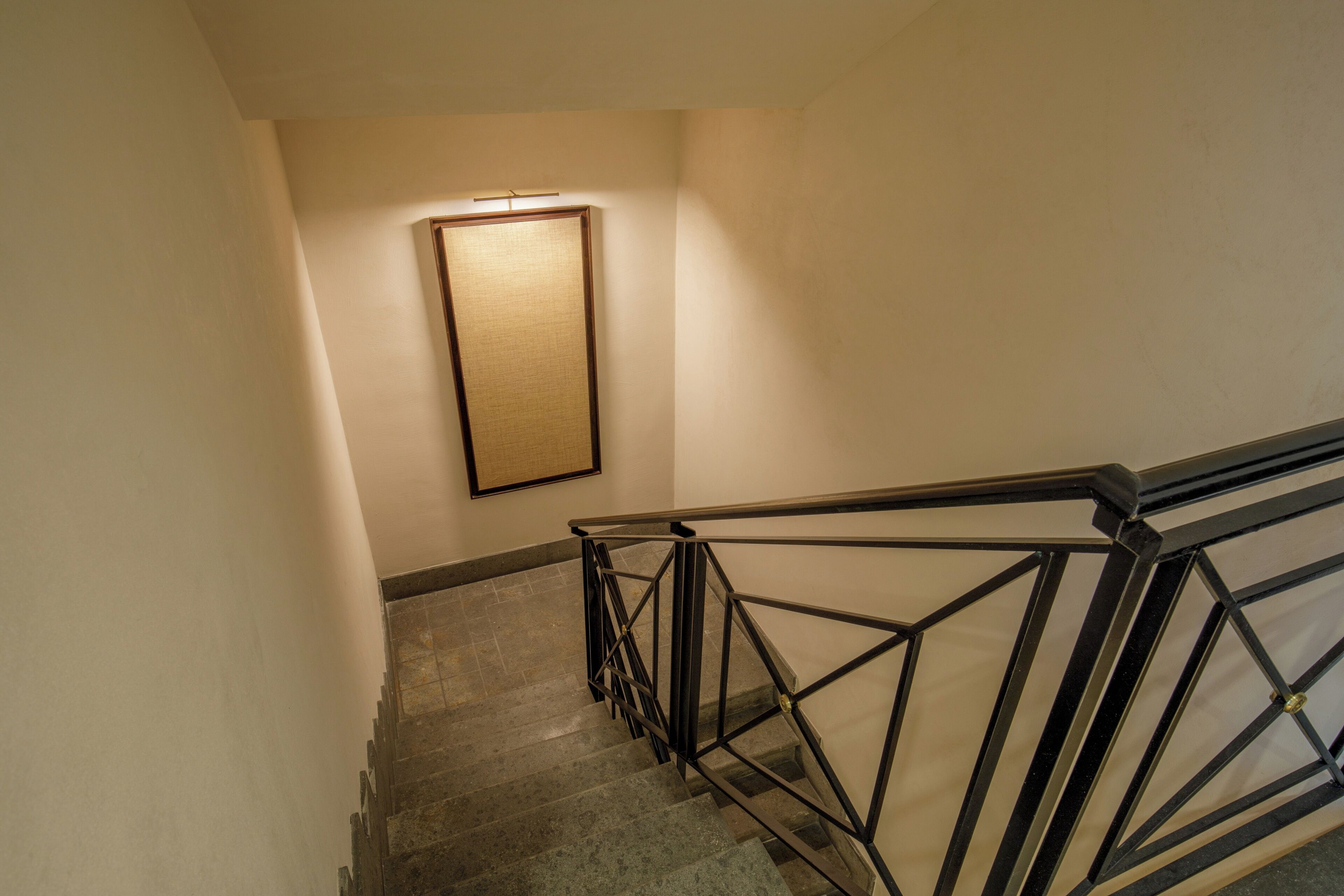 Una escalera con barandilla metálica de diseño geométrico y un cuadro en la pared.
