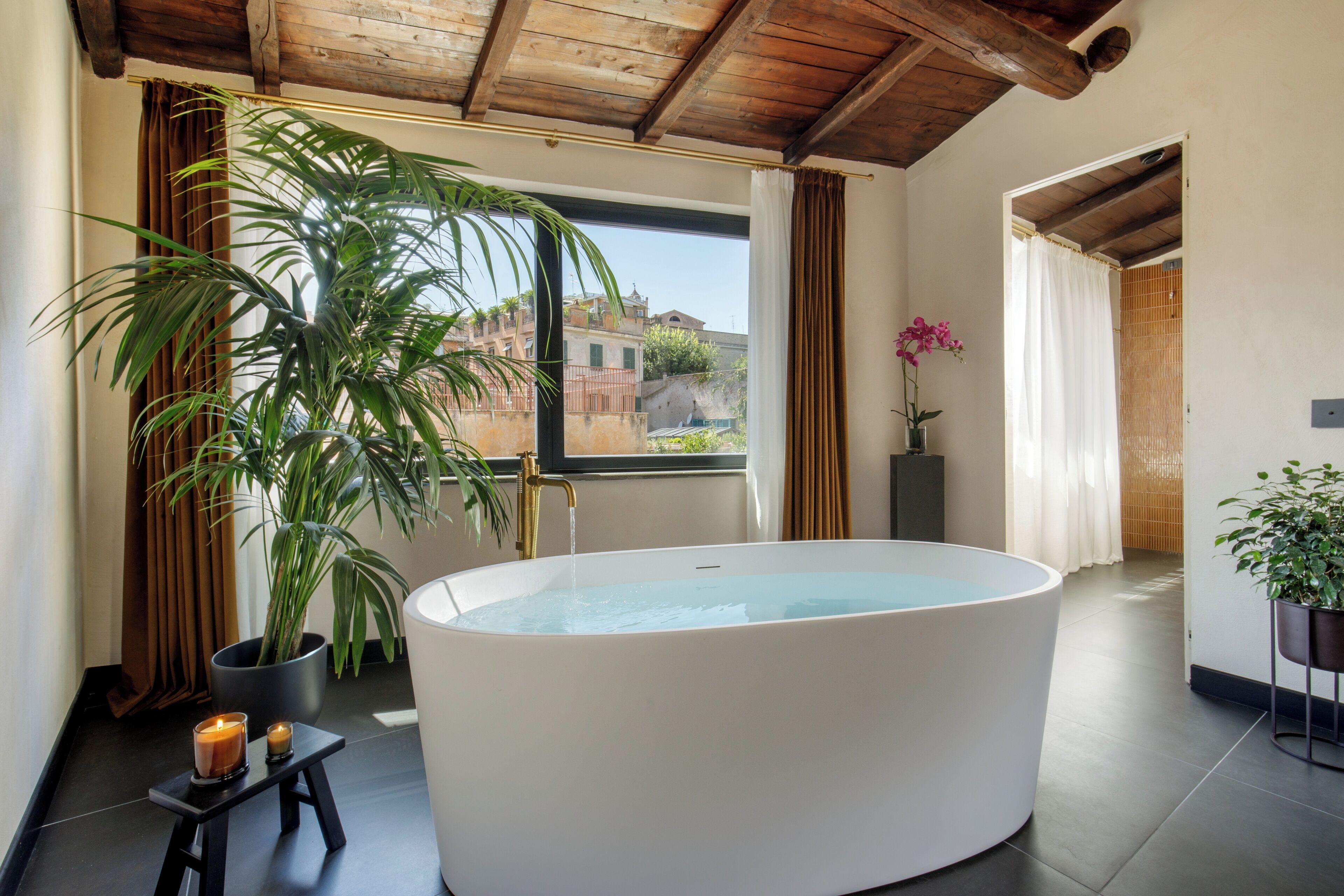 A modern bathroom with a freestanding bathtub, a potted plant, and a view of buildings outside.