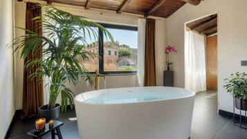 A modern bathroom with a freestanding bathtub, a potted plant, and a view of buildings outside.