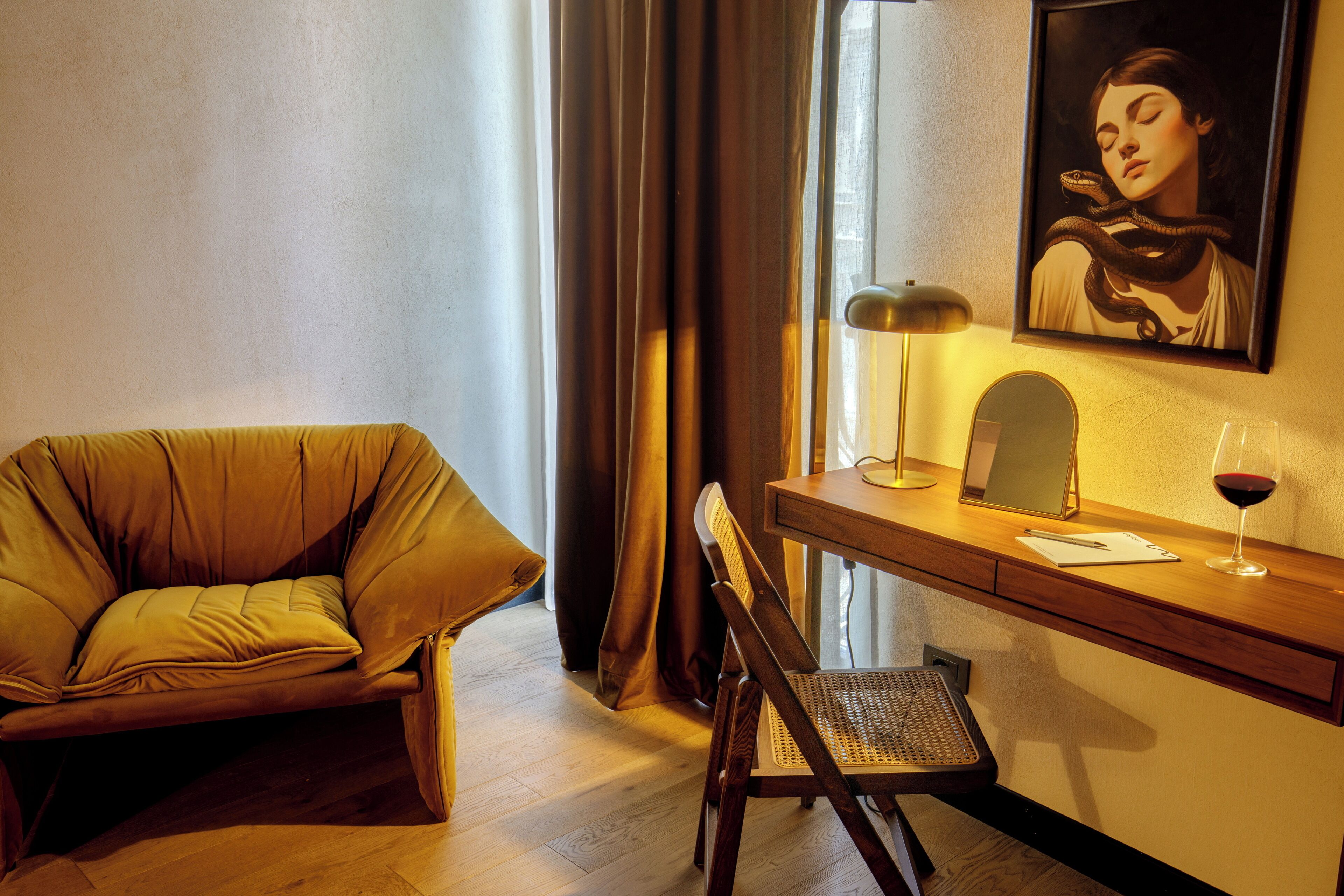 A room with a sofa, a desk, a chair, a lamp, a framed picture, and a glass of wine.