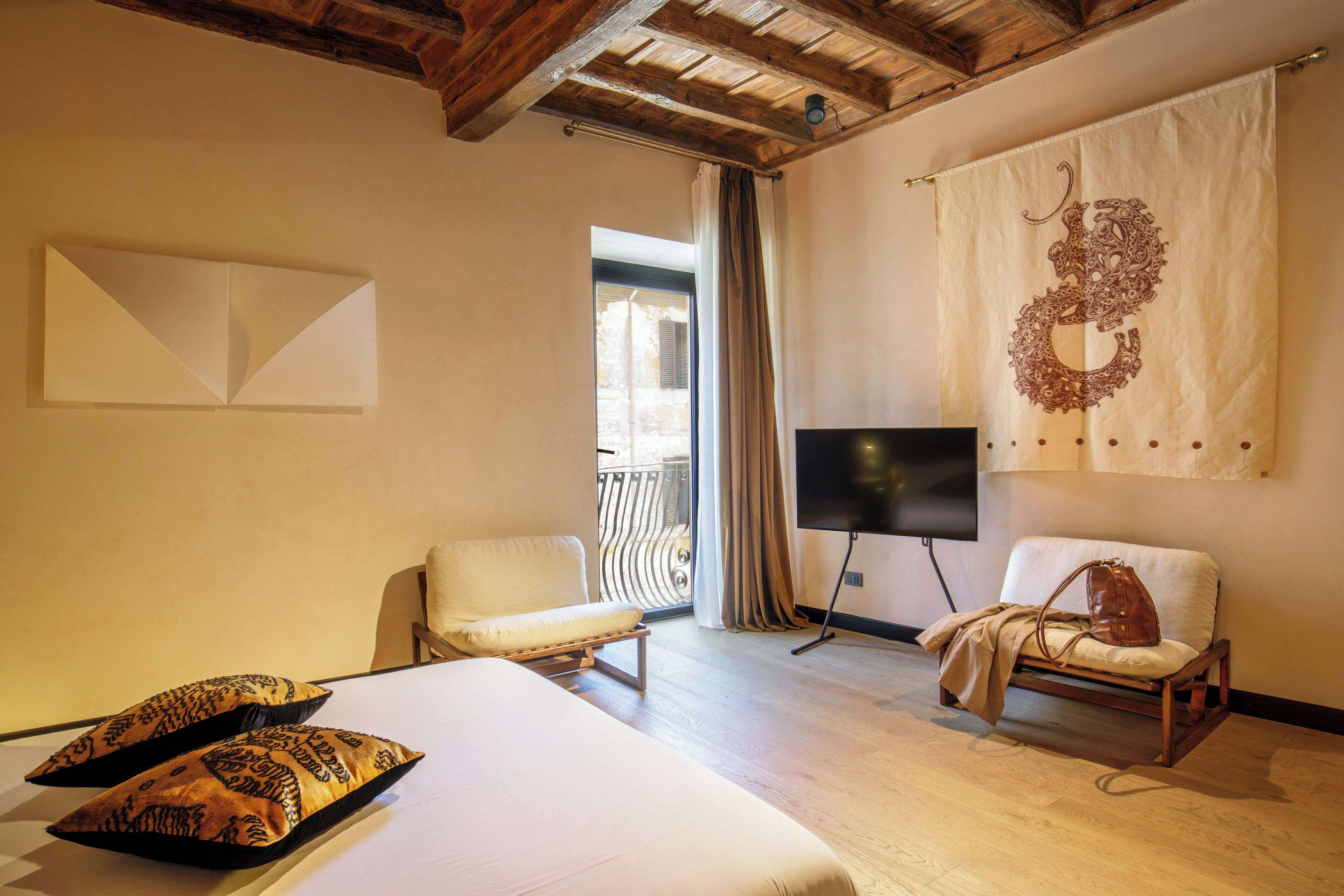 Hotelkamer met een bed, twee stoelen, een televisie en een balkon met gordijnen.