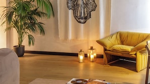 A cozy living room with a large tapestry, a potted plant, a yellow armchair, and a small table with a glass of wine. - Palazzo Serpe Suites near Colosseum (Rome)