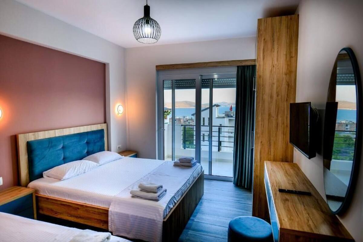 Habitación de hotel con cama, escritorio de madera, televisor y balcón con vistas.