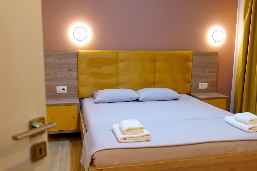 A hotel room with a wooden headboard, two bedside tables, a bed with white linens, and two wall-mounted lights.