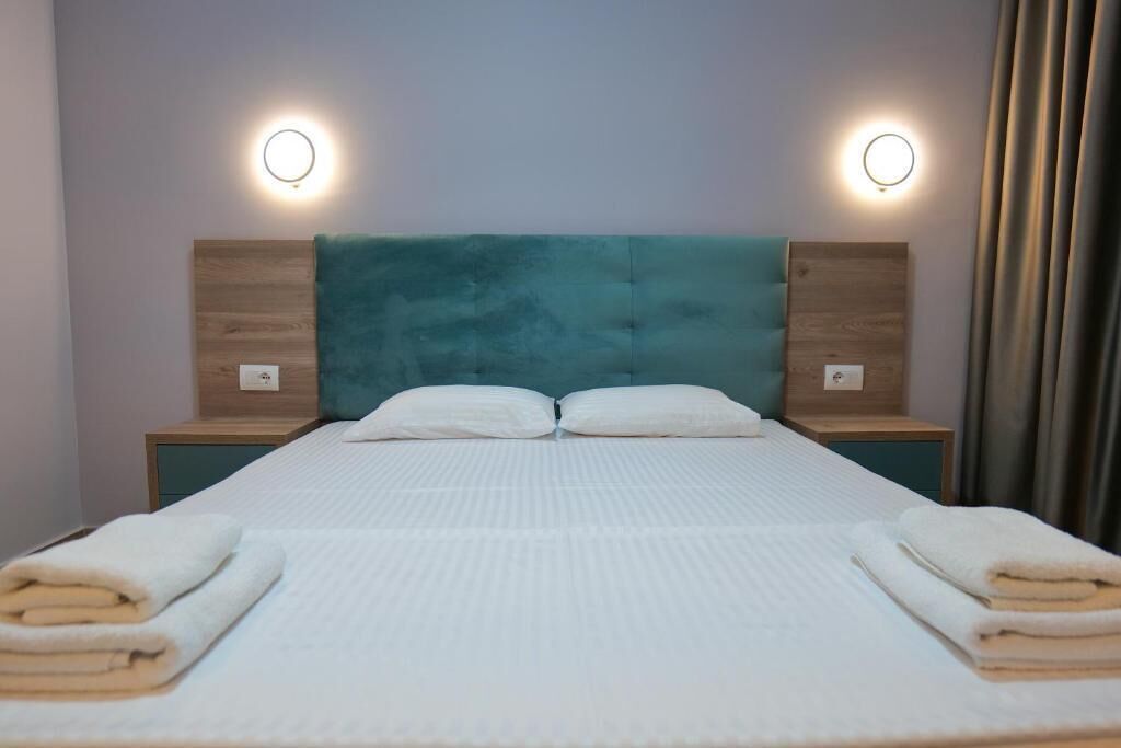 A neatly made bed with white bedding and two pillows, flanked by wooden nightstands with round wall lights.