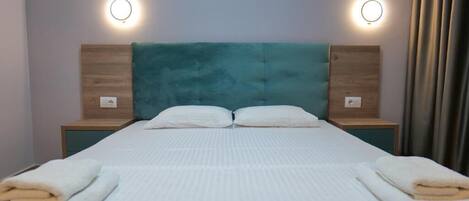 A neatly made bed with white bedding and two pillows, flanked by wooden nightstands with round wall lights.