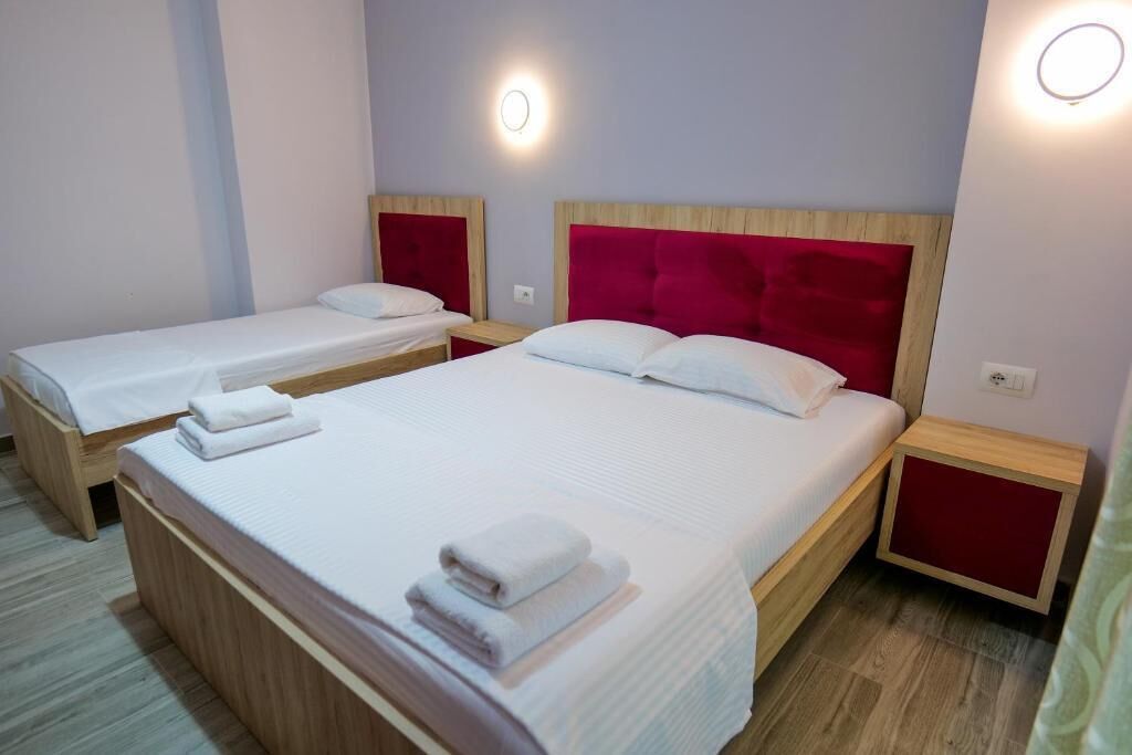 A hotel room with two single beds and a larger bed, all with white linens and red headboards.