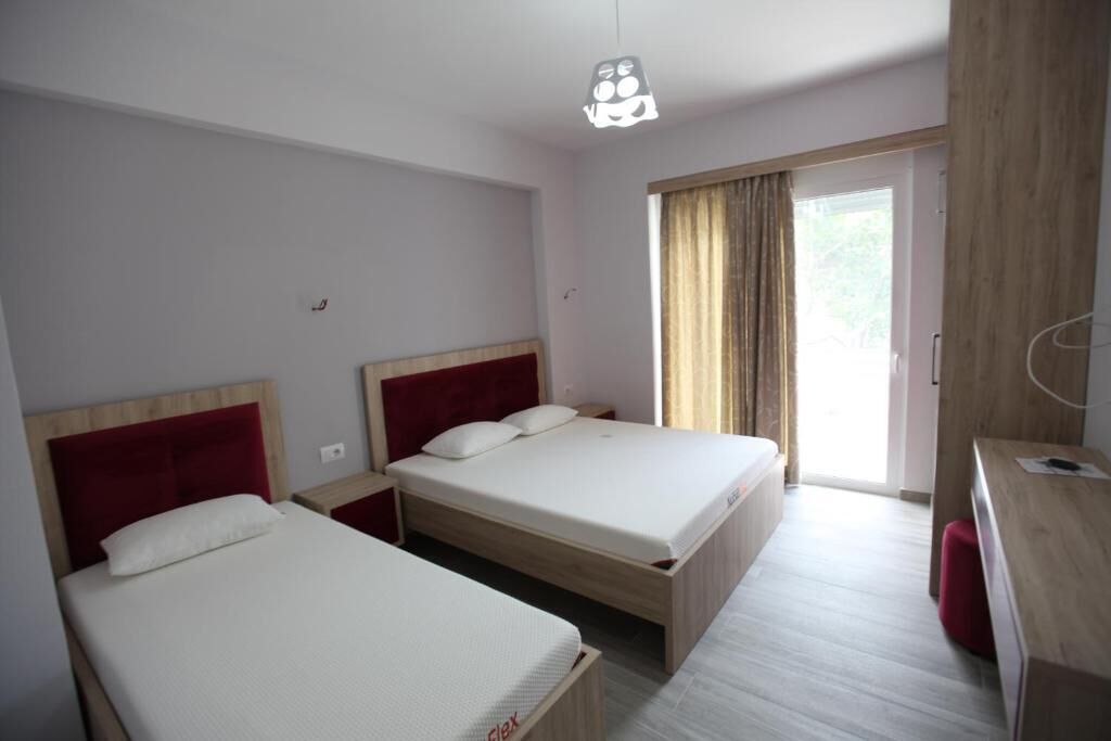 A hotel room with two beds, a wooden desk, and a window with curtains.
