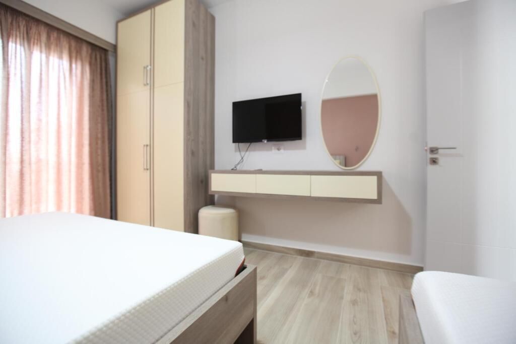 Ett hotellrum med en säng, en tv som är monterad på väggen, en spegel ovanför tv:n, ett trägolv och en dörr.