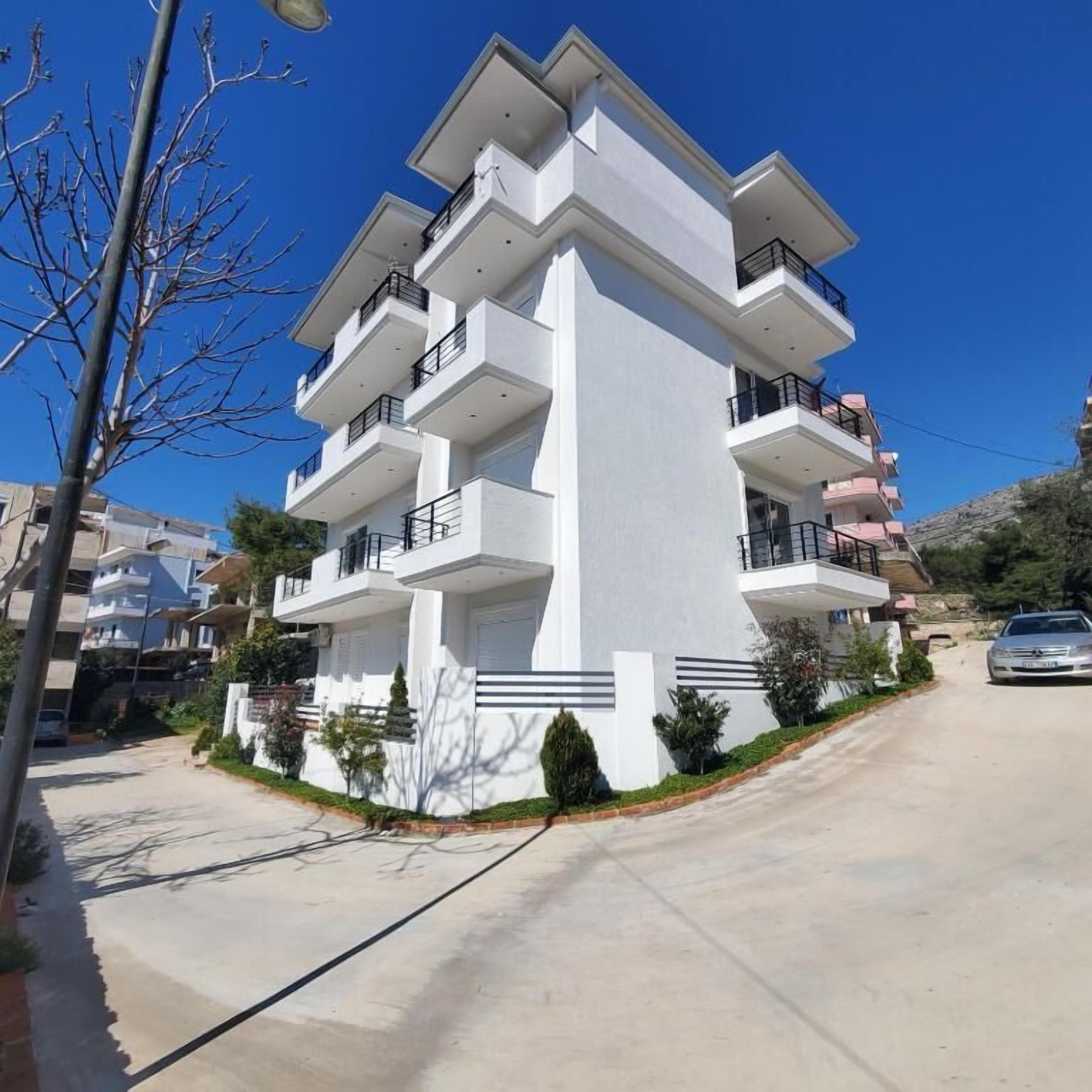 Un immeuble résidentiel moderne à plusieurs étages, doté de balcons, d’une allée et surplombant un ciel bleu dégagé.