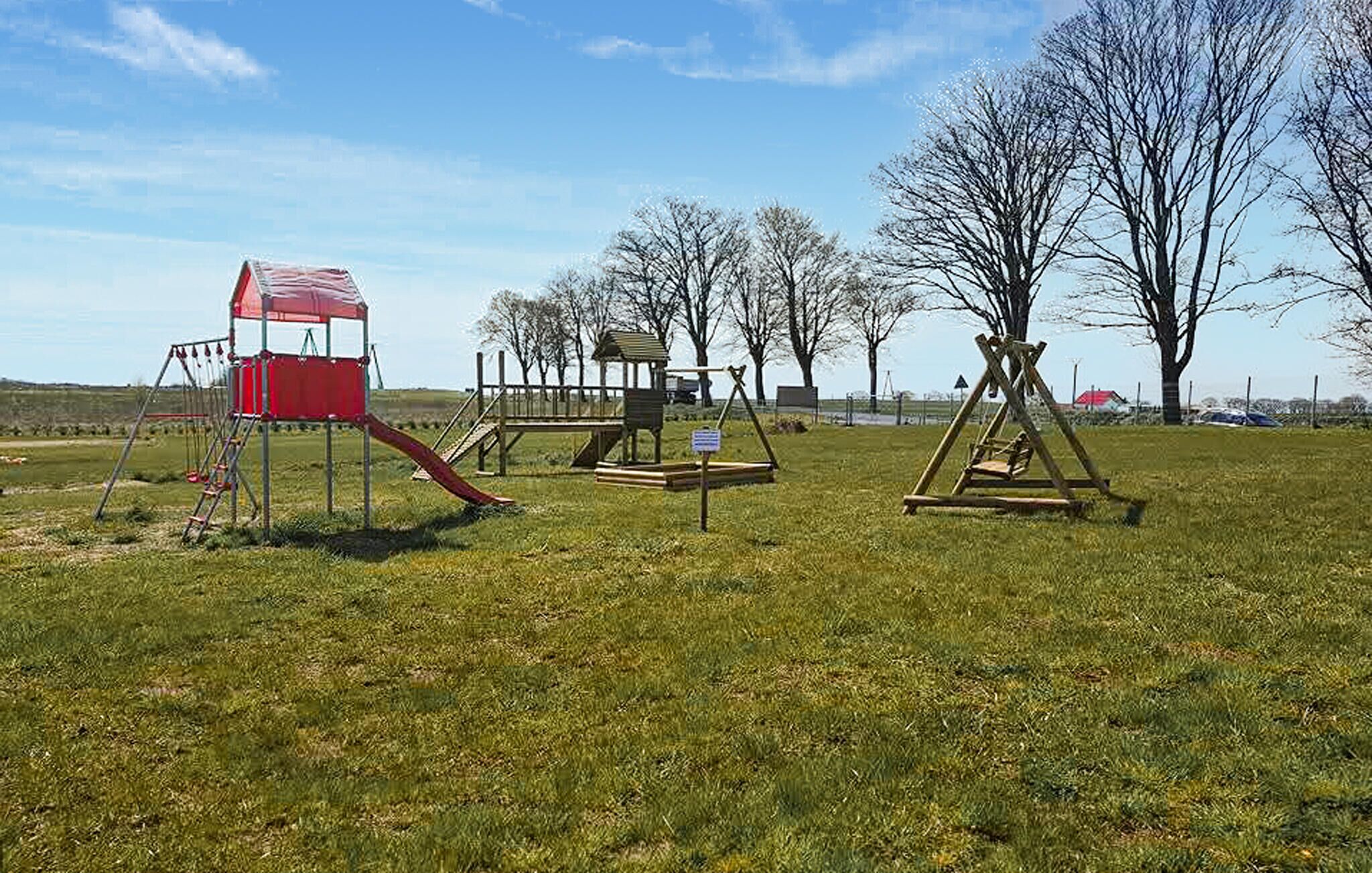 Un parque infantil con una estructura roja para escalar, columpios y un tobogán.