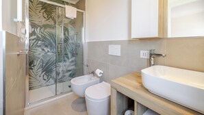 Un baño moderno con cabina de ducha de vidrio, un lavabo independiente, un lavamanos grande y un mueble de tocador de madera.
