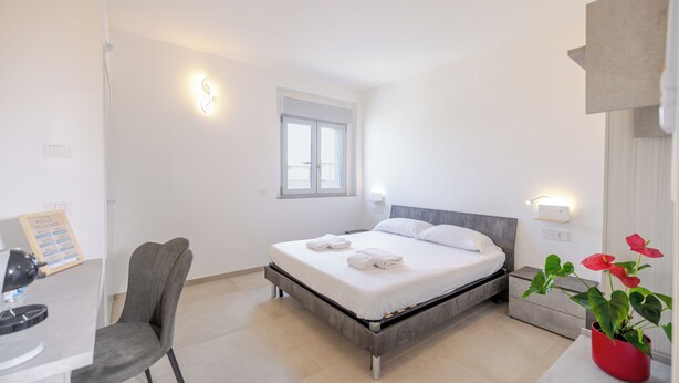 Un dormitorio con cama, escritorio, silla, ventana y planta.
