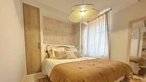 Quarto com uma cama grande, guarda-roupa de madeira, luminária de fibra e parede estampada.