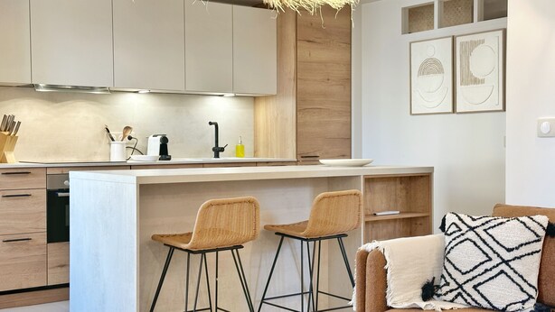 Cozinha moderna com ilha central, dois banquetes, sofá com almofadas estampadas e um vaso decorativo.
