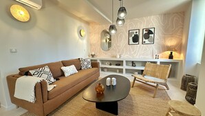 A modern living room with a brown sofa, a round coffee table, a wicker chair, and a white console table with shelves. - Le Saint-Nazaire (Sanary-sur-Mer)