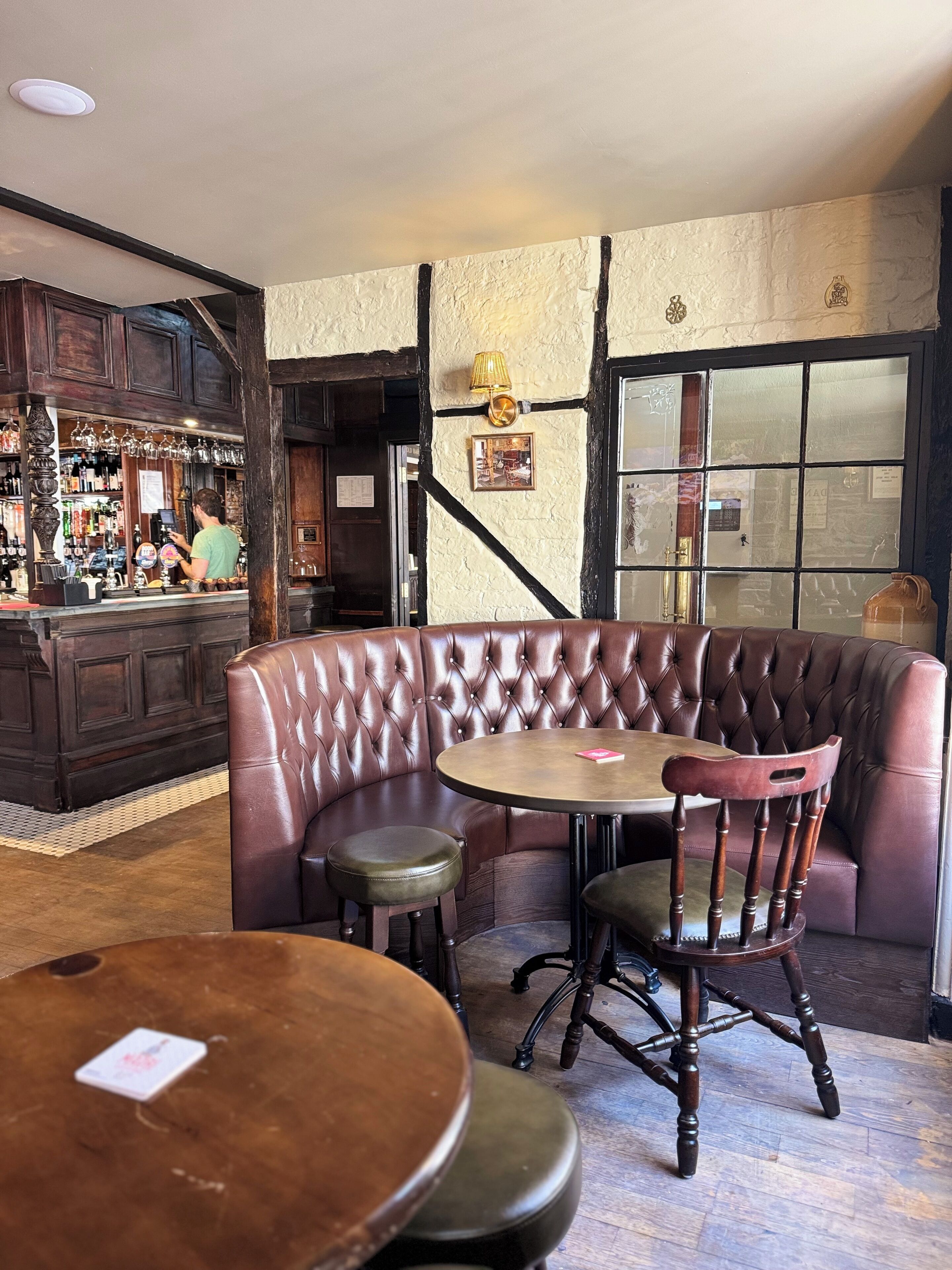 Un rincón acogedor de bar con una barra de madera, un taburete y una mesa redonda con una silla.