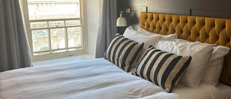 A hotel room with a large bed, a tufted headboard, and a view of a building through a window.