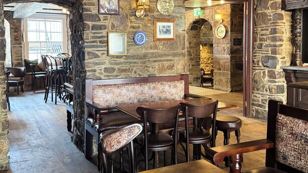 A stone-walled interior with a bar area, wooden tables and chairs, and framed pictures on the walls. - The Black Lion Hotel  (Cardigan)