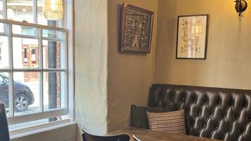 A cozy corner with a leather booth, wooden chairs, and a table. A chalkboard with writing is on the wall, and a framed playing card hangs above.