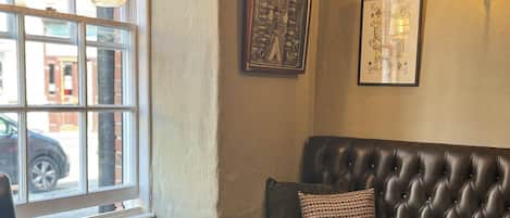 Un coin accueillant avec un banc en cuir, des chaises en bois et une table. Un tableau noir avec des inscriptions est accroché au mur, et une carte à jouer encadrée est suspendue au-dessus.
