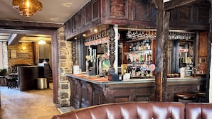A bar area with a stone wall, wooden bar counter, and various bottles and glasses. - The Black Lion Hotel  (Cardigan)
