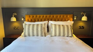 A neatly made bed with striped pillows, a tufted headboard, and wall-mounted lamps. - The Black Lion Hotel  (Cardigan)