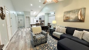 A spacious living area with a dark-colored sofa, patterned ottoman, and a blue and white patterned rug. A ceiling fan and recessed lighting are visible. - Side by Side Condos Walk-in Lake View Top Floor Next to SDC (Reeds Spring)