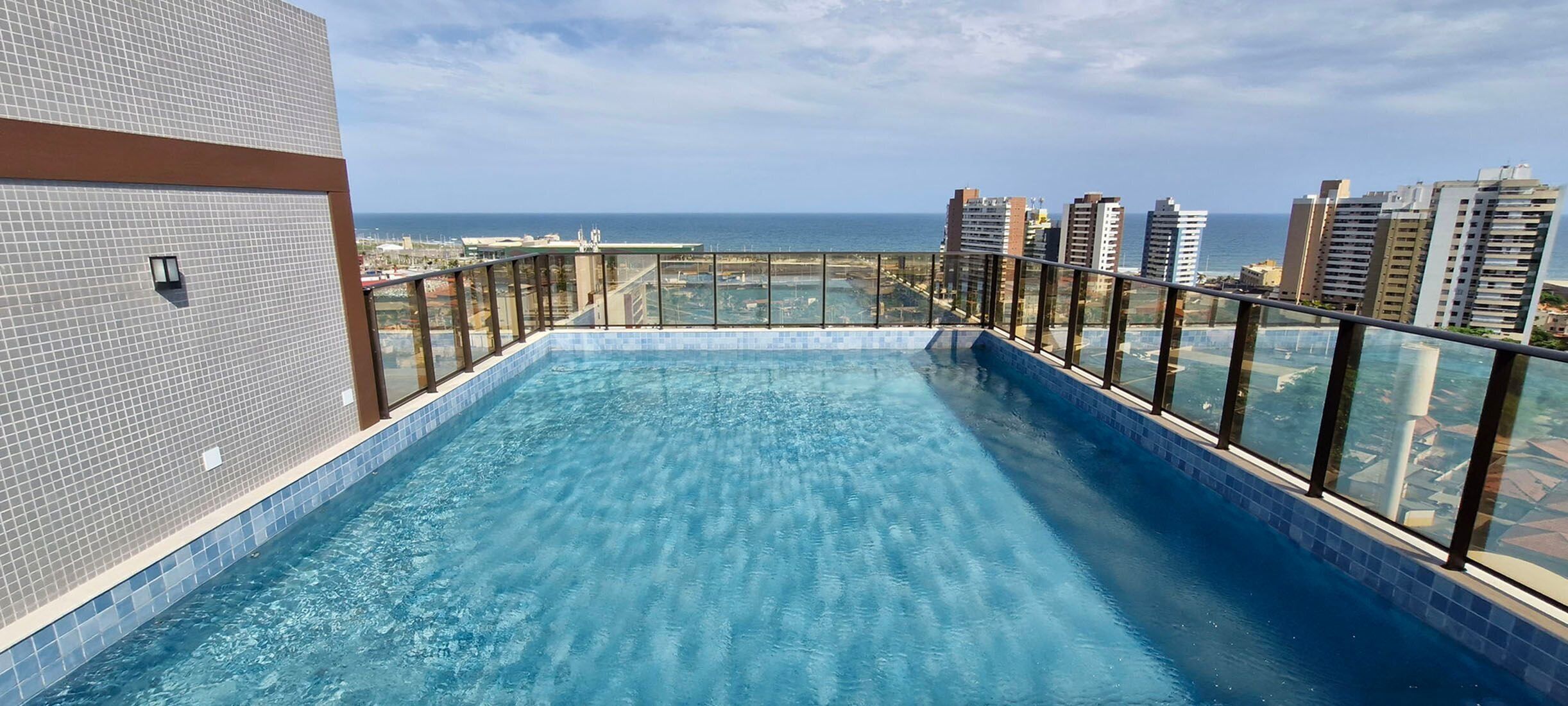 A rooftop infinity pool with a glass barrier, offering a view of the ocean and surrounding buildings.