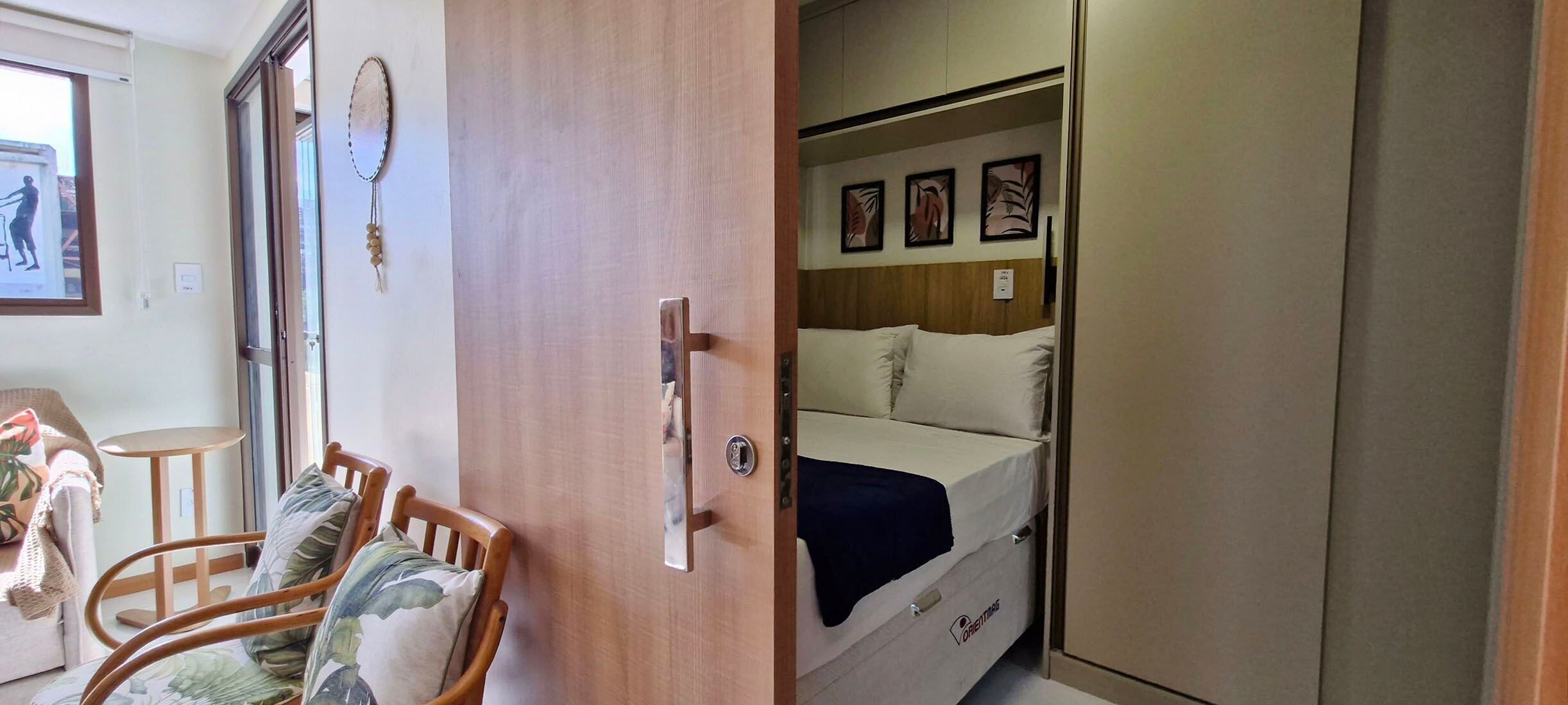 A compact room with a bed, a wooden wardrobe, a small table, and a chair.