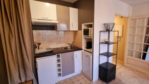 A compact kitchen with white cabinets, a microwave, and a black shelf unit. - Apartment in Biarritz (Biarritz)