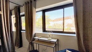 A room with a bed, a desk with a lamp, and a view of a building outside. - Apartment in Biarritz (Biarritz)