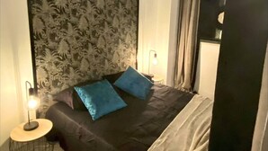 A bedroom with a large bed, two pillows, a headboard with a leaf pattern, a bedside lamp, and a window with curtains. - Apartment in Biarritz (Biarritz)