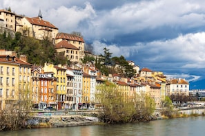 A riverside cityscape with historic buildings, a bridge, and a castle-like structure. - Les M Riers in Grenoble (Grenoble)
