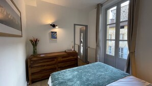 A bedroom with a bed, a dresser, a framed picture, a vase with flowers, and a window with curtains. - Les M Riers in Grenoble (Grenoble)