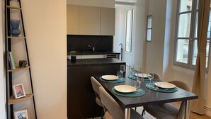A modern kitchen with dark countertops and white cabinets, a dining table set with plates and glasses, and a bookshelf with framed pictures. - Les M Riers in Grenoble (Grenoble)