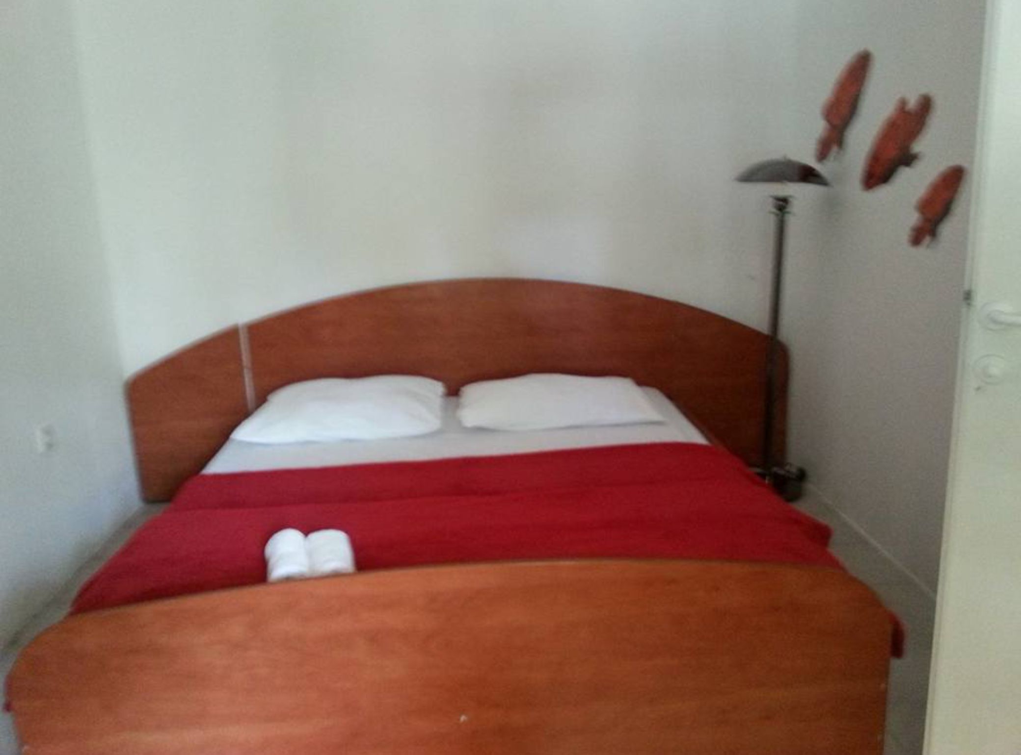 Ein Einzelbett mit Holzvorhang, weißen Kissen und einer roten Decke.