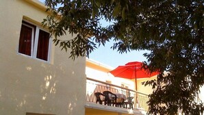 Edifici de dues plantes amb un balcó al pis superior, que inclou un para-sol vermell i mobiliari exterior.