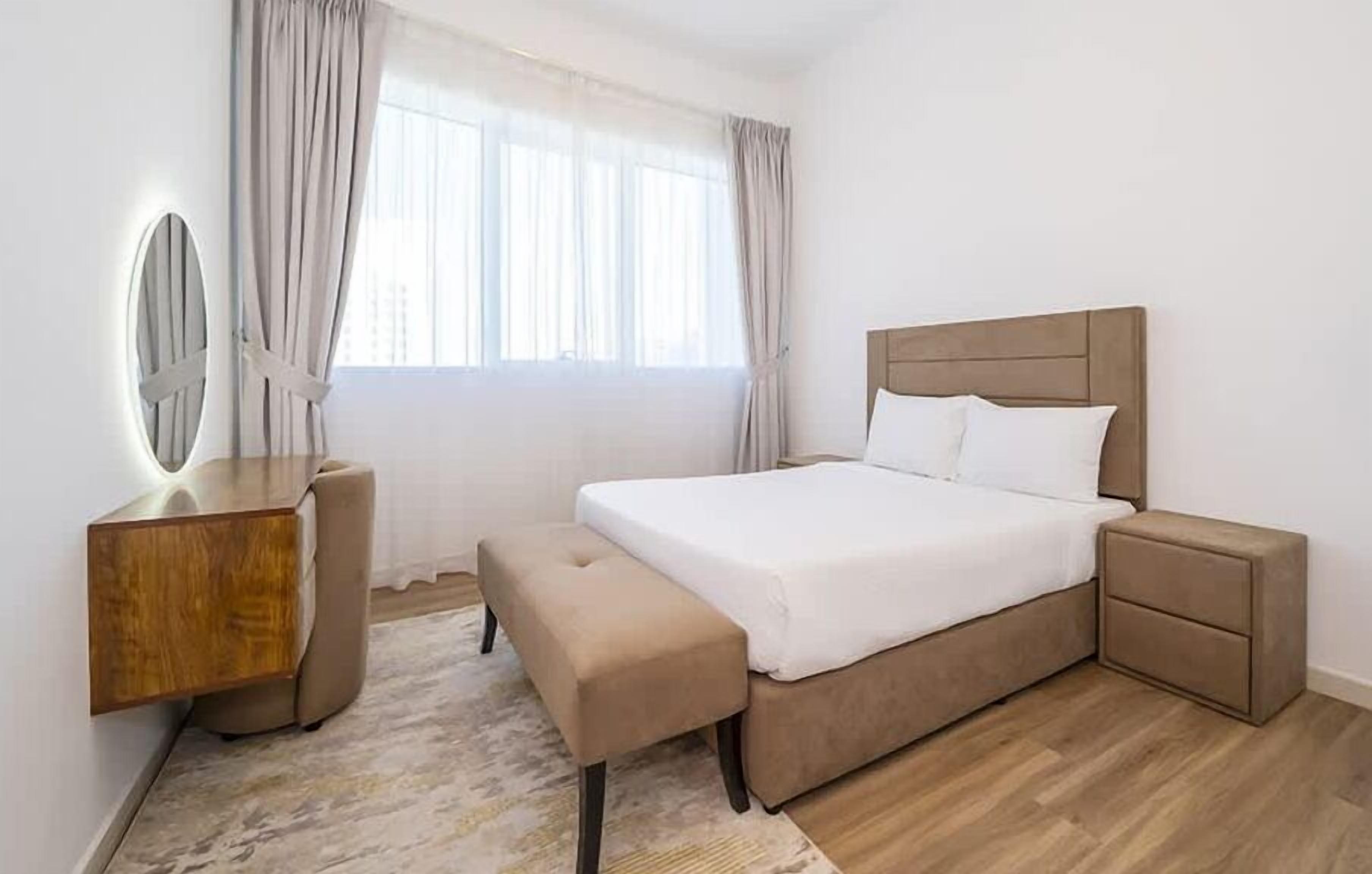 Une chambre à coucher comprenant un lit, des tables de chevet, une coiffeuse avec un miroir et un banc.